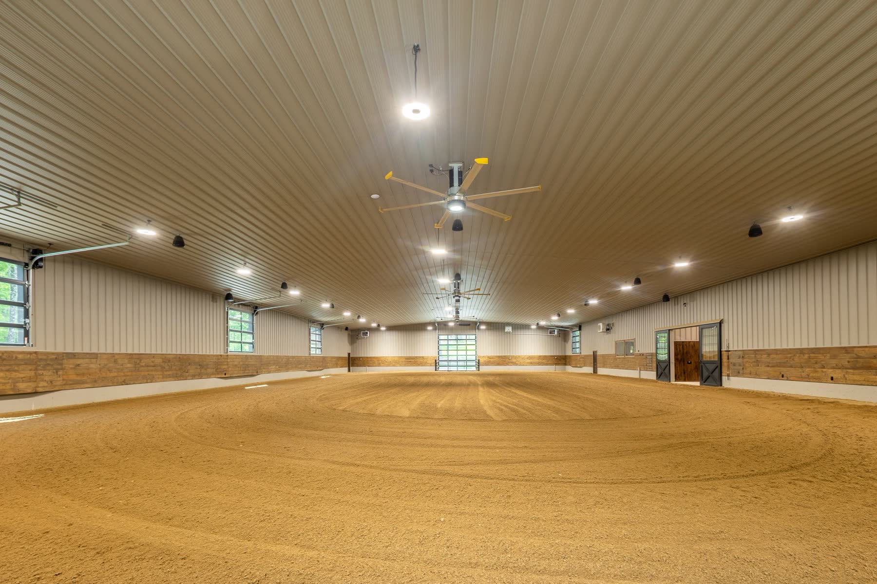Indoor riding arena with overhead fans and skylights
