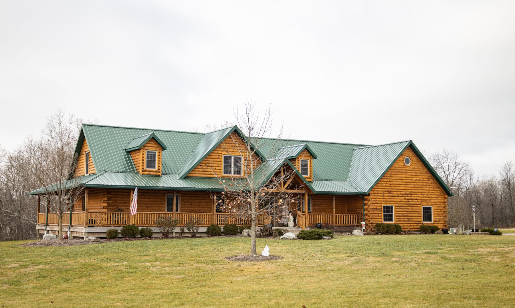 Log home with green metal roof and wraparound porch